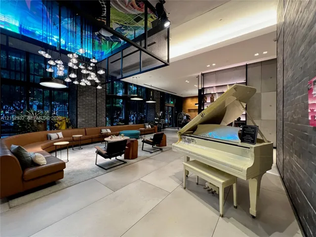 Expansive lobby featuring large-format tile flooring, exposed dark brick walls, floor-to-ceiling windows, and a tiered multi-pendant lighting installation