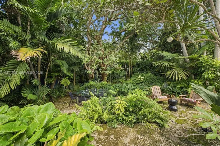 Naturalized landscaping featuring established tropical flora, mature trees, and irregular stone paving