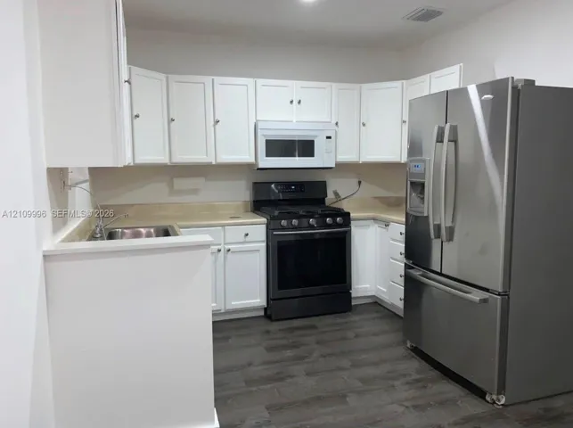 Kitchen featuring white cabinetry, wood-finish flooring, a stainless steel refrigerator, a built-in microwave, and a black gas range