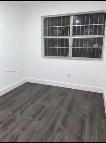 Neutral-toned wood-finish flooring and bright white walls featuring a window with integrated decorative metal security bars