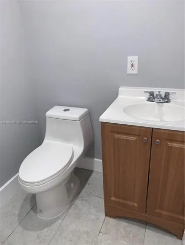 Bathroom featuring a wood-finish vanity with a white integrated countertop, chrome dual-handle faucet, one-piece toilet, and tile flooring