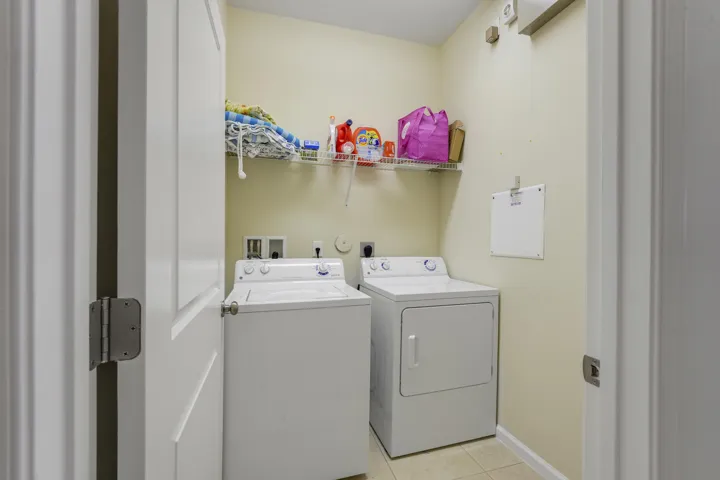 Laundry area featuring dedicated washer and dryer hookups, wire shelving, and neutral tile flooring