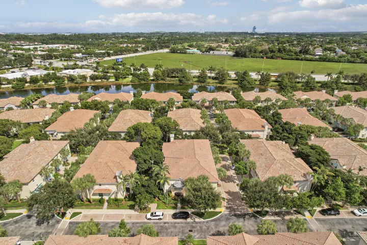 Aerial perspective of a multi-unit residential community featuring terracotta-style roof tiles, paved thoroughfares, interspersed mature landscaping, and a central water feature
