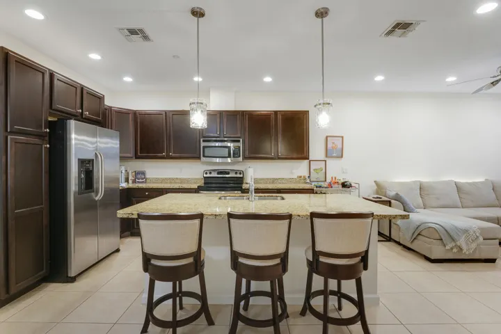 Kitchen featuring dark wood-finish cabinetry, stone countertops, central island with integrated sink, stainless steel appliances, and recessed lighting