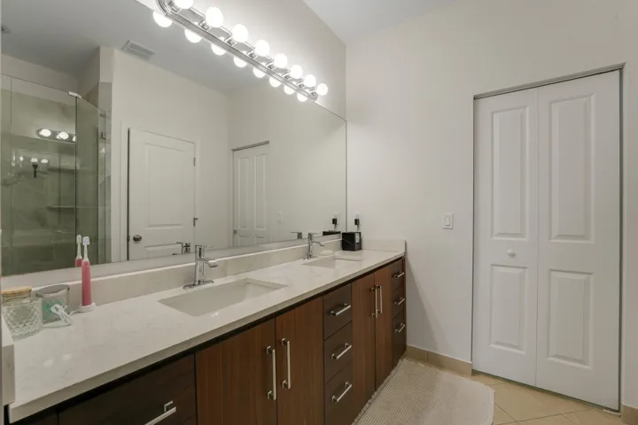 Dual-sink vanity with stone-finish countertop, dark wood-finish cabinetry, full-width mirror, and glass-enclosed shower stall