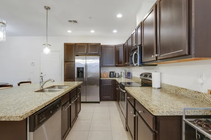 Kitchen featuring dark-finish cabinetry, stone-surface countertops, stainless steel appliances, a center island with a dual-basin sink, and recessed lighting