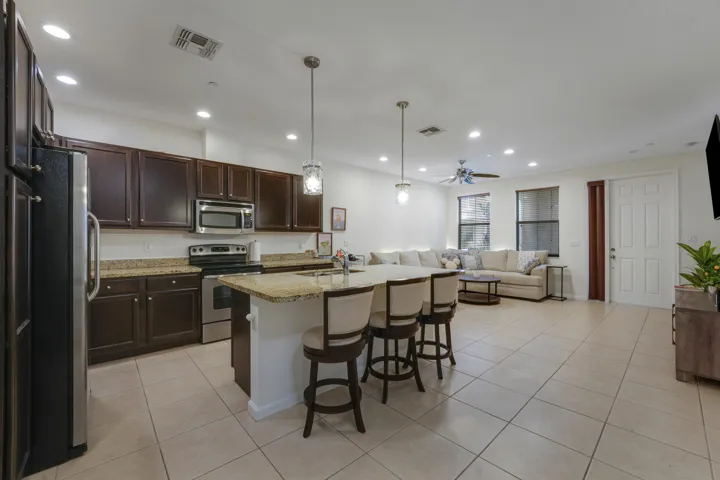 Open-concept kitchen featuring dark wood cabinetry, stone countertops, a central island with bar seating, stainless steel appliances, and tile flooring