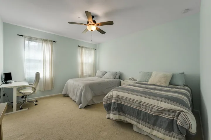 Neutral-toned interior featuring wall-to-wall carpeting, dual windows with installed curtain rods, and a ceiling fan with integrated lighting