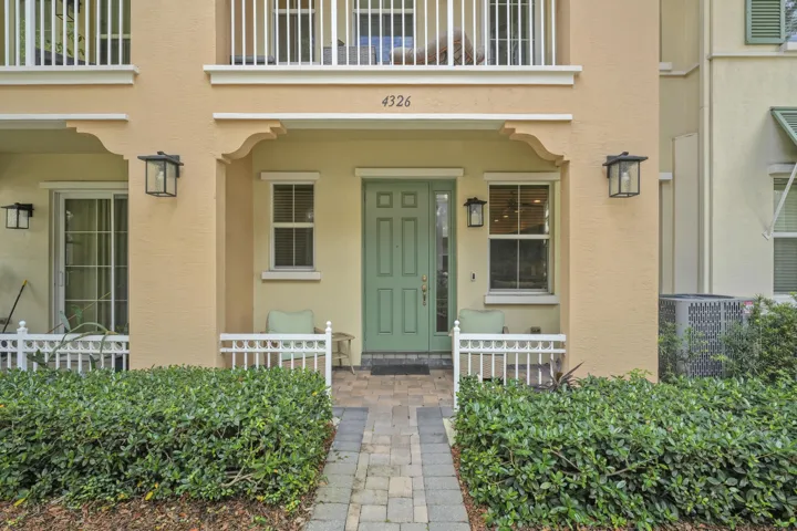 Covered entryway featuring a paver walkway, green six-panel door with sidelight, decorative exterior corbels, and wall-mounted lantern fixtures