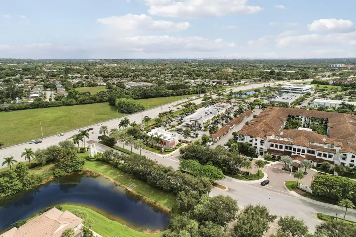 Aerial perspective featuring a multi-story building with a clay tile roof, a central courtyard, and a prominent water feature surrounded by established palm trees and manicured landscaping