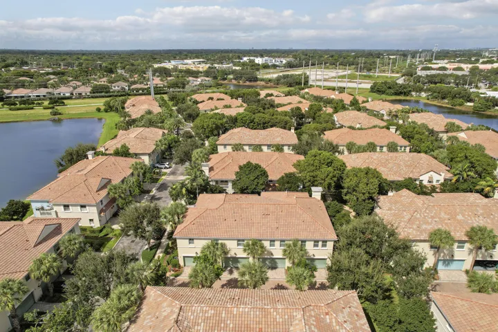 Aerial perspective of a multi-unit residential complex featuring clay tile roofing, light-toned stucco exteriors, attached multi-car garages, and surrounding waterfront scenery