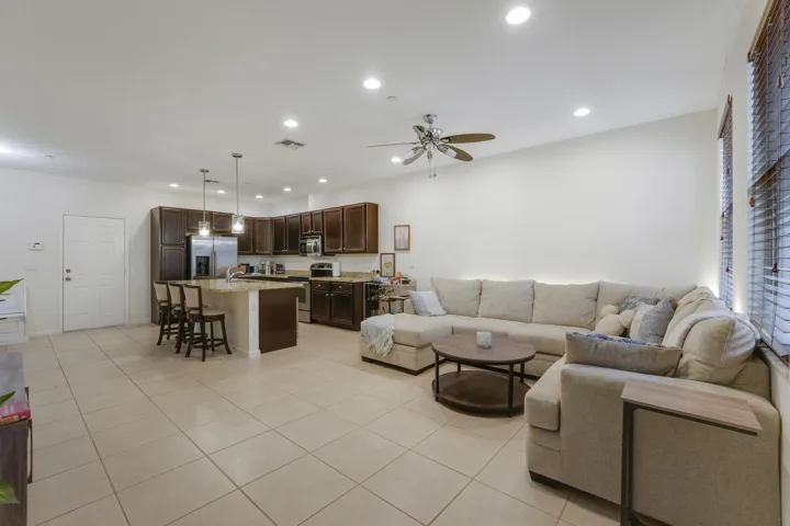 Open-concept interior featuring large-format tile flooring, recessed ceiling lighting, kitchen island with stone countertop, dark wood cabinetry, and a ceiling fan