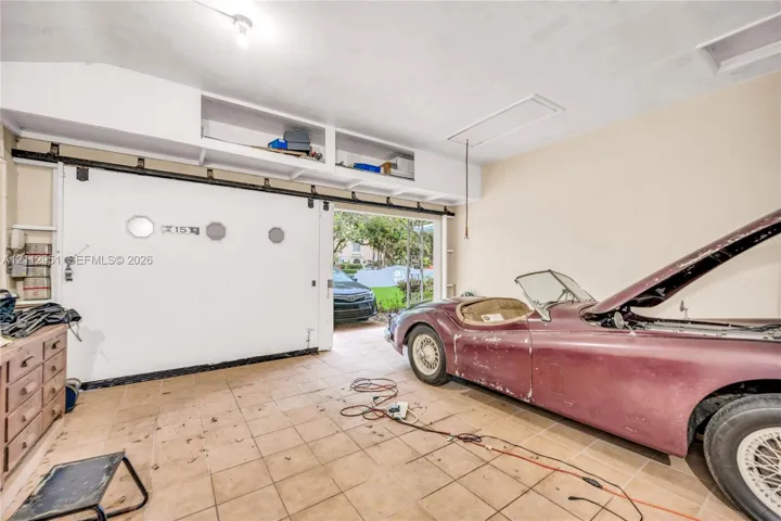 Enclosed garage featuring tile flooring, built-in overhead storage cabinetry, and a large sliding door with integrated circular accents