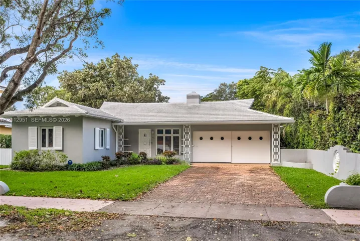 Single-story exterior featuring a light-toned tile roof, decorative geometric masonry accents, a brick-paved driveway, a two-car garage with circular windows, and shutter-framed windows