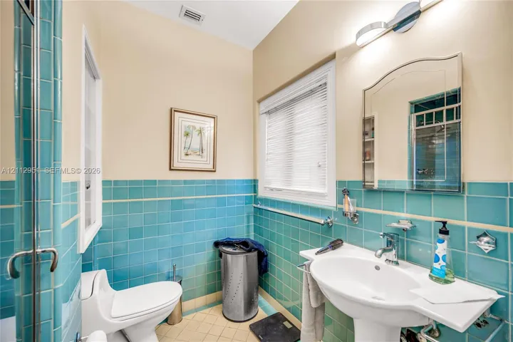 Bathroom featuring turquoise ceramic wall tile, a white pedestal sink, a chrome faucet, and a frameless mirror