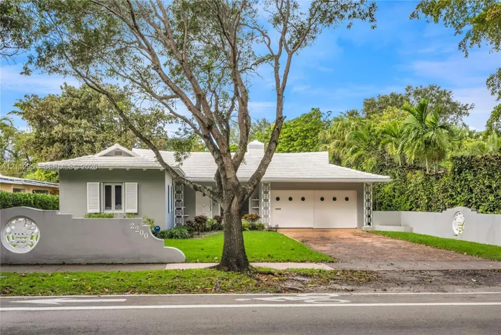 Single-story exterior featuring a tile roof, decorative concrete privacy wall with circular lattice accents, attached garage with porthole windows, and shuttered window treatments