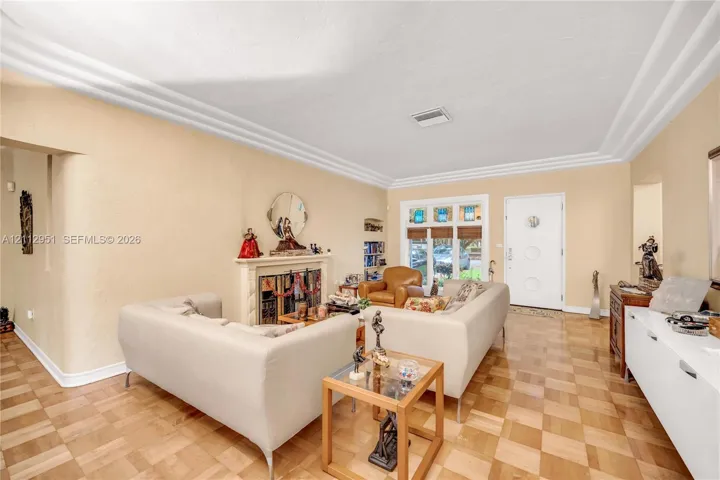 Parquet wood flooring, crown molding, stone fireplace surround, and recessed entryway door with integrated circular glass accents