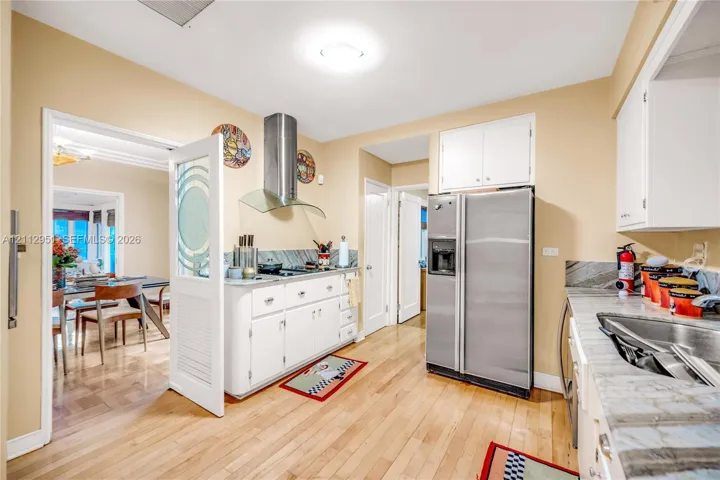Kitchen featuring wood-finish flooring, white cabinetry, stainless steel refrigerator, stainless steel chimney-style range hood, and stone-finish countertops