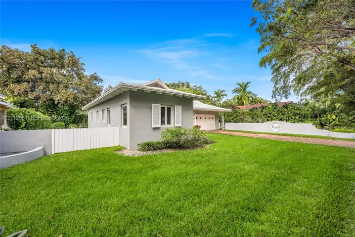 Stucco exterior with decorative shutters, multi-car garage, brick-paver driveway, and fenced perimeter