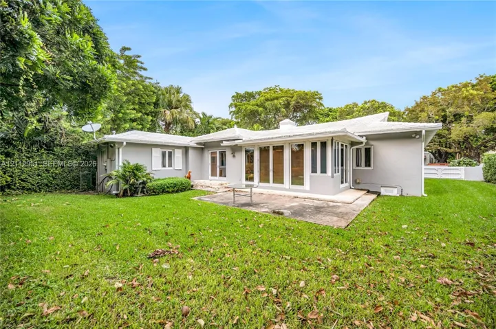 Exterior rear elevation featuring a light-toned masonry facade, expansive green lawn, concrete patio, and multi-panel glass doors