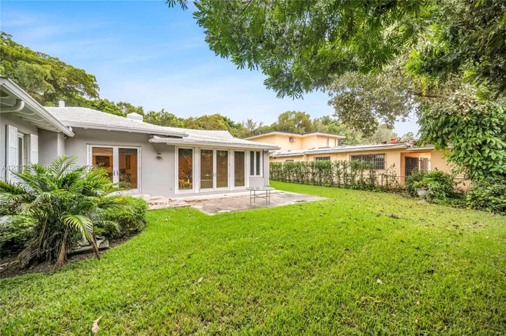 Private backyard featuring a manicured lawn, stone-paver patio, multi-panel glass doors, and mature landscaping