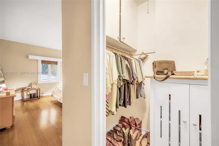 Walk-in closet featuring white built-in cabinetry, upper shelving, and a stone-surface countertop, complemented by wood-finish flooring in the room exterior