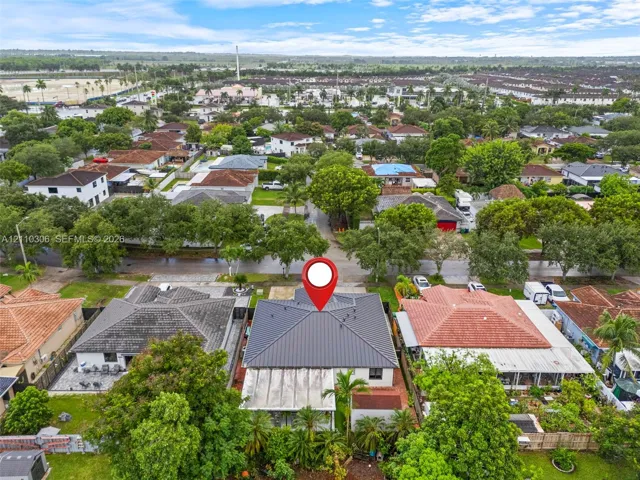 Aerial perspective of a residence featuring a dark-toned hipped roof, a rear covered patio, and established perimeter landscaping