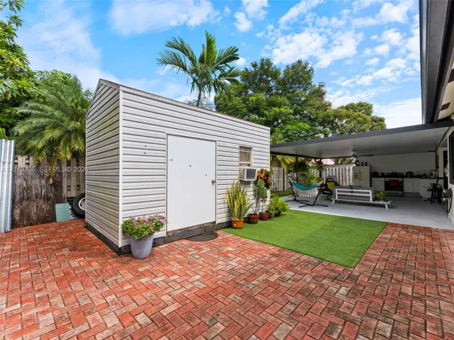 Rear exterior space featuring a herringbone-patterned brick patio, synthetic turf area, covered lanai, and detached storage structure