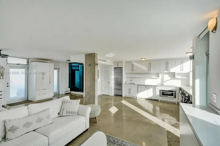 Open-concept interior featuring polished concrete flooring, white cabinetry, stainless steel appliances, and a central structural concrete pillar