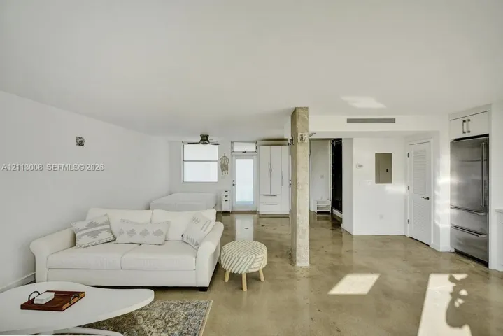 Polished concrete flooring, exposed concrete structural column, stainless steel refrigerator, and custom white cabinetry