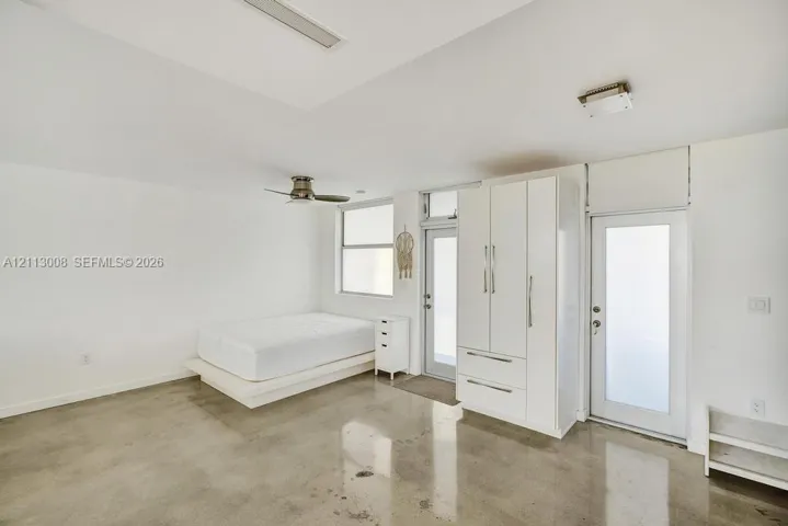 Polished concrete flooring, built-in white wardrobe cabinetry, ceiling fan, and frosted-glass panel doors