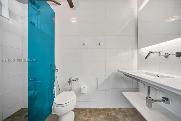 Bathroom featuring large-format white tile walls, a translucent blue glass shower partition, a wall-mounted floating vanity with integrated sink, and polished metal wall-mounted faucet hardware