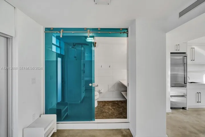 Sliding blue-tinted glass door featuring a stainless steel track system, white wall tiling, stone-finish flooring, and built-in shelving