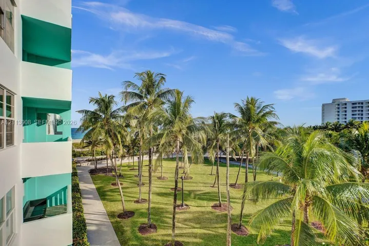 Multi-story exterior with private balconies featuring teal-accented walls, overlooking an expansive grass courtyard with mature palm trees