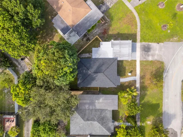 Aerial perspective featuring a shingled roof, a covered outdoor patio area, and mature trees on a landscaped lot