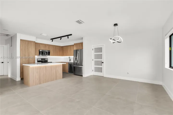 Kitchen featuring wood-finish cabinetry, a central island with a quartz countertop, stainless steel appliances, matte black track lighting, and large-format tile flooring