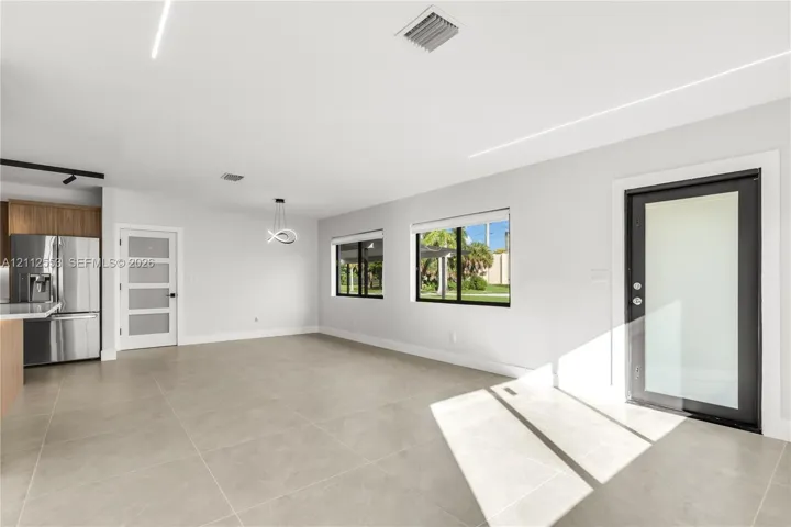 Open-concept interior featuring large-format tile flooring, modern linear recessed lighting, a stainless steel refrigerator, and a contemporary entry door with a glass pane