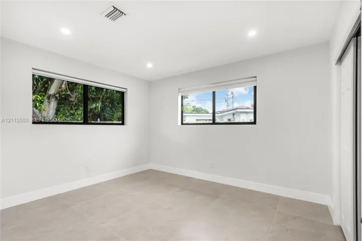 Neutral-toned interior featuring large-format tile flooring, recessed ceiling lighting, and windows with black frames