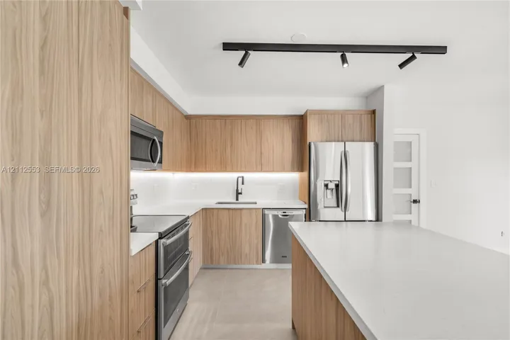 Kitchen featuring wood-finish cabinetry, quartz countertops, stainless steel appliances, under-cabinet lighting, and track lighting