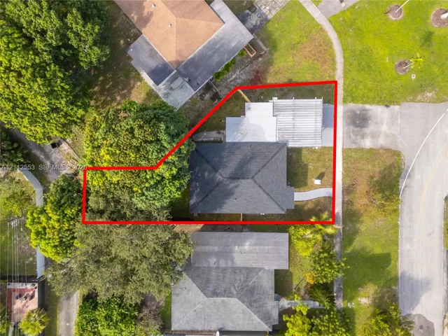 Aerial perspective showcasing a residential lot with a dark-shingled roof, attached pergola, concrete walkway, and mature trees