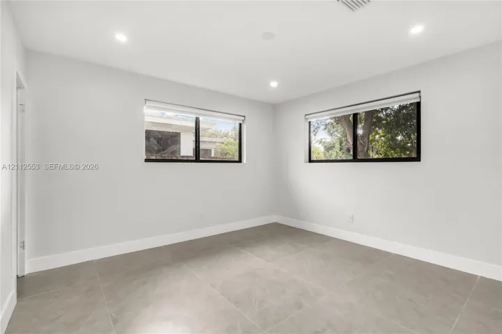 Neutral-toned room featuring large-format tile flooring, dual windows with black frames, recessed ceiling lighting, and smooth-finish walls