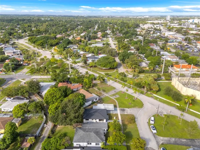Aerial perspective featuring a residential setting with mature trees, green space, palm foliage, and paved street infrastructure