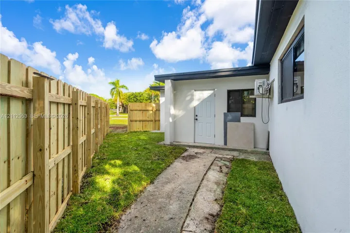 Stucco exterior wall with a wood privacy fence, concrete walkway, and window with dark trim