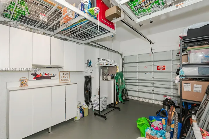 Garage featuring white built-in wall cabinetry, stone-surface countertop, and overhead mounted metal storage racks