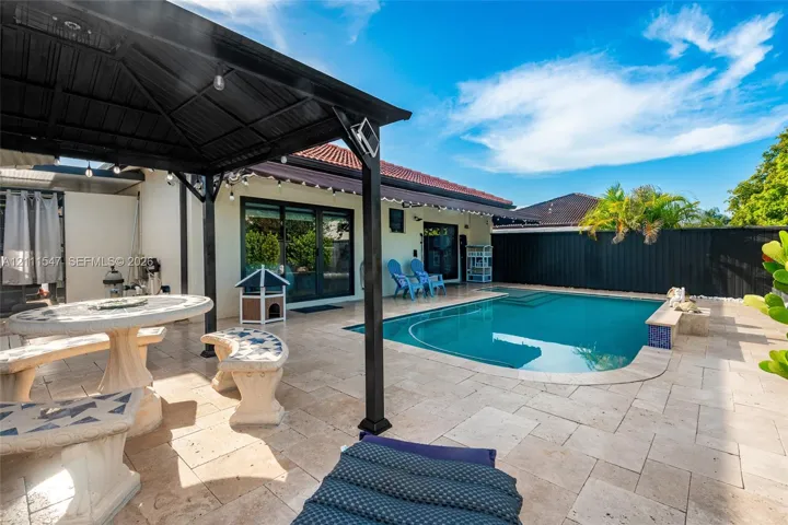 Outdoor living space featuring a hardscaped stone patio, a covered metal gazebo, and an in-ground pool with a perimeter fence