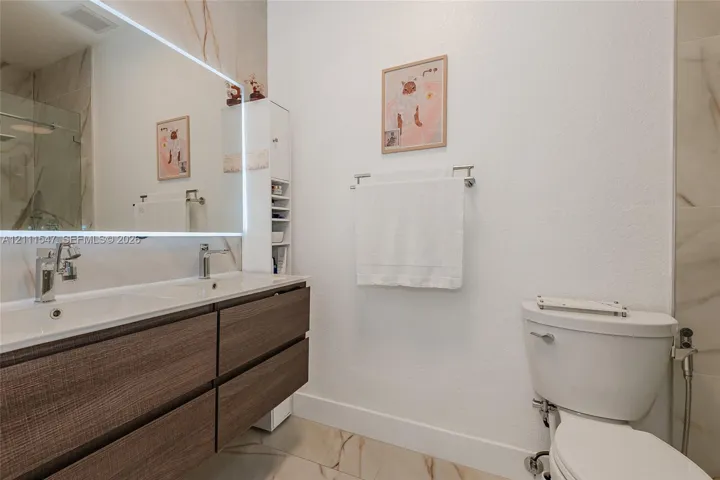 Double-vanity with a wood-finish floating cabinet, large LED-backlit mirror, integrated sink basins, polished metal faucets, and large-format tile flooring