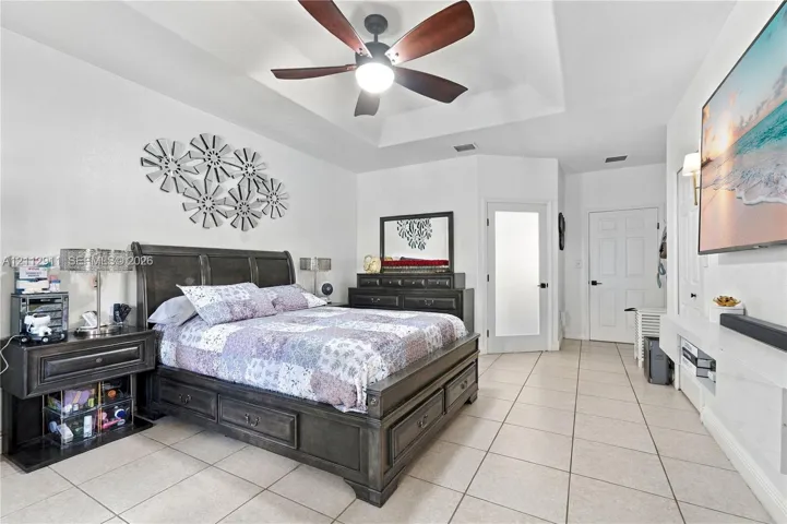 Tray ceiling with a central multi-blade ceiling fan, neutral tile flooring, and frosted glass paneled door