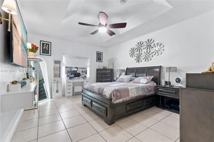 Tray ceiling featuring a central lighted ceiling fan, complemented by tile flooring, an arched mirror installation, and wall-mounted lighting fixtures