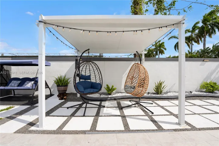 Outdoor patio featuring a white pergola, large-format concrete pavers, decorative gravel inlay, and a perimeter stucco wall