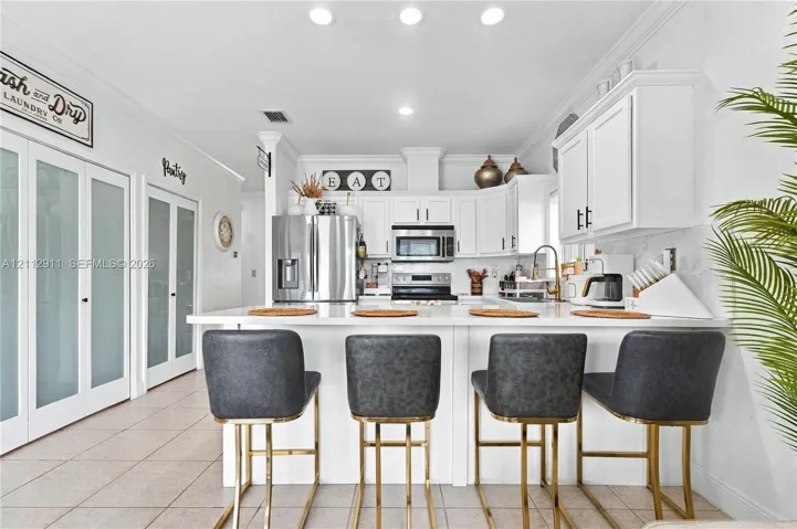 Kitchen featuring white cabinetry, solid-surface countertops, stainless steel appliances, recessed lighting, and dual frosted-glass pantry doors